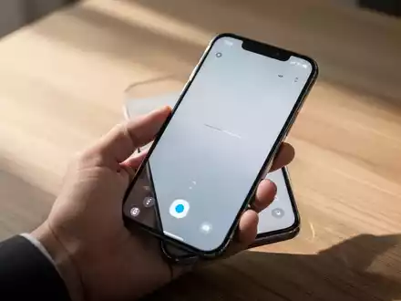 Ein modernes Premium-Smartphone in einer Hand, das eine minimalistische Benutzeroberfläche auf einem Holztisch zeigt. - Foto: über boerse-global.de