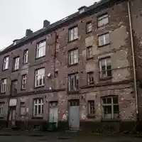 Ein sanierungsbedürftiges Wohngebäude in einem Industriegebiet unter einem bewölkten Himmel. - Foto: über boerse-global.de
