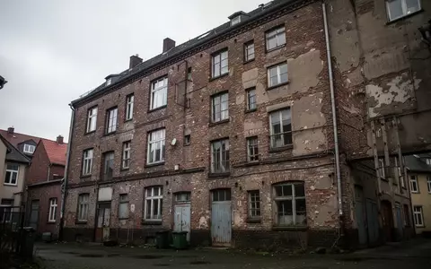 Ein sanierungsbedürftiges Wohngebäude in einem Industriegebiet unter einem bewölkten Himmel. - Foto: über boerse-global.de