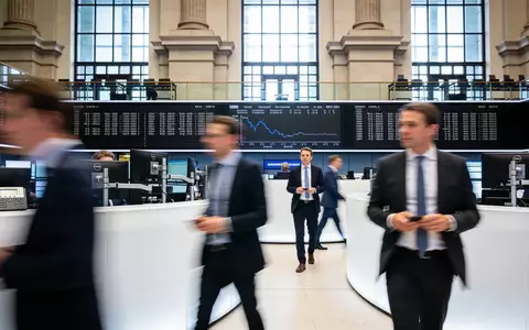 Bewegte Szene auf dem Frankfurter Börsenparkett mit Börsenhändlern vor einer neutralen Hintergrundarchitektur. - Foto: über boerse-global.de