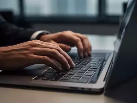 Nahaufnahme einer Person, die an einem Laptop in einem professionell beleuchteten Büro arbeitet. - Foto: über boerse-global.de
