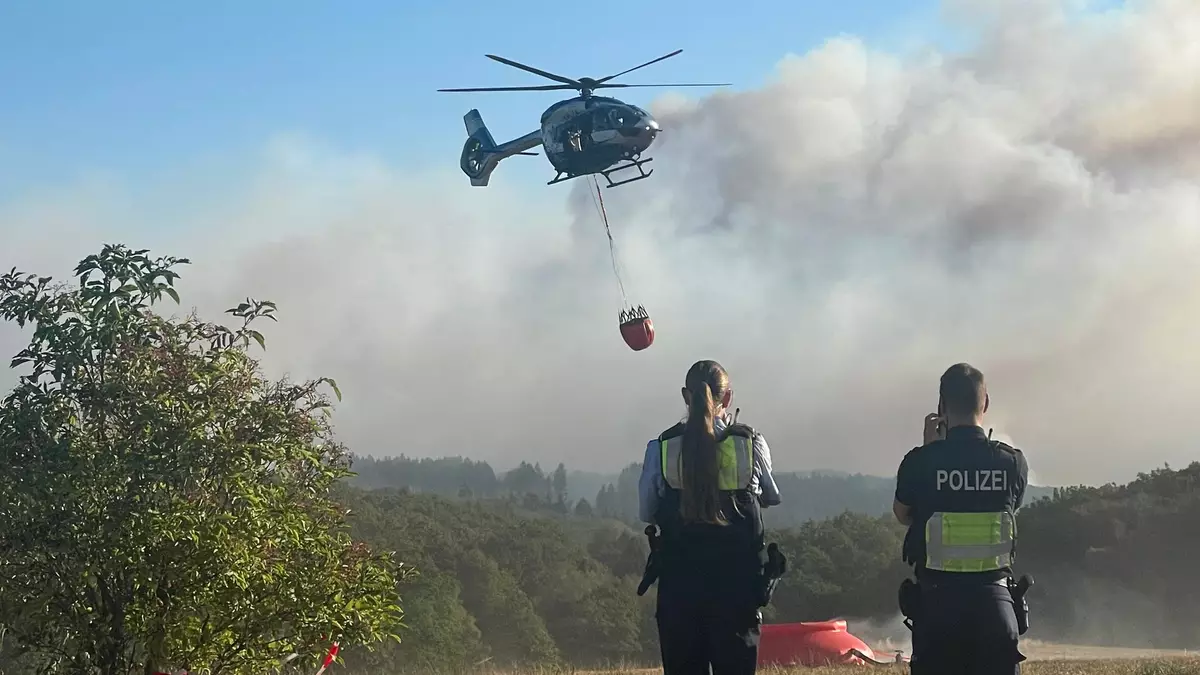 Ein Löschhubschrauber fliegt an. - Bild: Christoph Driessen/dpa