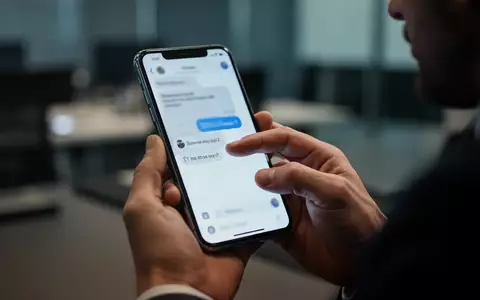 Person hĂ€lt ein Smartphone in einer professionellen Umgebung, wĂ€hrend sie eine Nachricht auf dem Bildschirm prĂŒft. - Foto: ĂŒber boerse-global.de