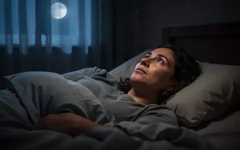 Eine Person liegt nachts wach in einem abgedunkelten Schlafzimmer und blickt ruhig zur Decke. - Foto: über boerse-global.de
