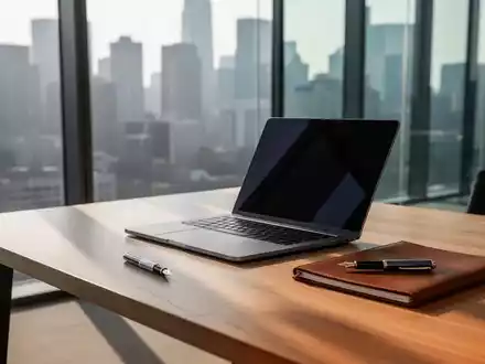 Ein minimalistischer Büroschreibtisch mit Laptop und Notizbuch vor einer Fensterfront mit Blick auf eine Skyline. - Foto: über boerse-global.de