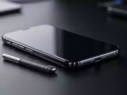 Ein modernes Smartphone liegt auf einem dunklen Schreibtisch in einer professionellen, technologischen Arbeitsumgebung. - Foto: über boerse-global.de