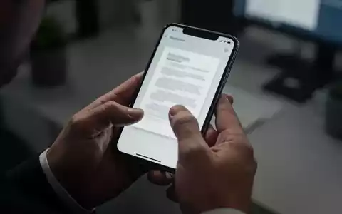 Hände halten ein Smartphone, auf dessen Bildschirm ein Dokument angezeigt wird, in einer Büroumgebung. - Foto: über boerse-global.de