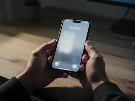 Nahaufnahme einer Person, die in einem dunklen Büro besorgt auf ihr Smartphone schaut, während sie Online-Banking nutzt. - Foto: über boerse-global.de