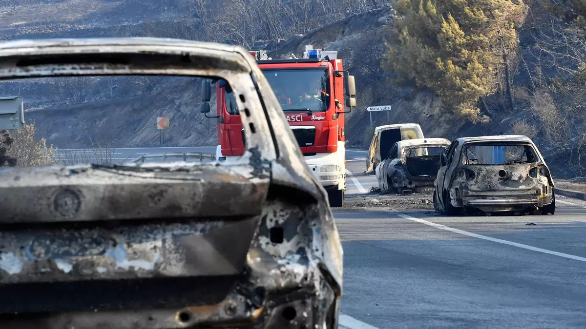 Ein Feuerwehrfahrzeug fährt nach einem Waldbrand an der kroatischen Adria zwischen ausgebrannten Autos hindurch. - Bild: Josko Ponos/AP/dpa