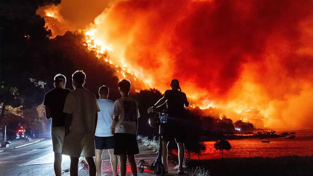 Menschen beobachten am frühen Freitag, dem 14. August 2026, einen Waldbrand an der Adriaküste in der Nähe von Omis im Süden Kroatiens. - Bild: Tom Dubravec/AP/dpa