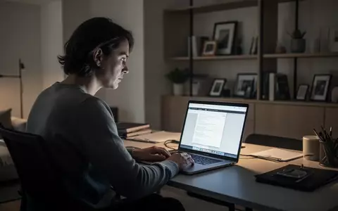 Eine Person sitzt an einem Schreibtisch vor einem Laptop und blickt nachdenklich auf den Bildschirm in einem modern beleuchteten Raum. - Foto: über boerse-global.de