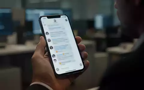 Eine Person hĂ€lt ein Smartphone in der Hand, wĂ€hrend sie in einer bĂŒroĂ€hnlichen Umgebung sitzt. - Foto: ĂŒber boerse-global.de