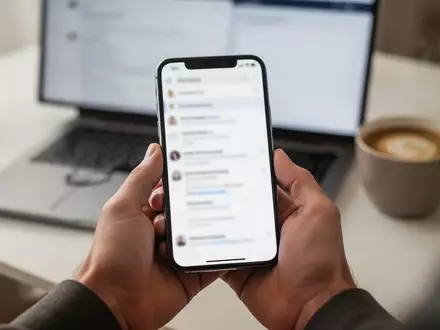 Nahaufnahme einer Hand mit einem Smartphone vor einem unscharfen Schreibtischhintergrund als Symbol für digitale Sicherheit. - Foto: über boerse-global.de