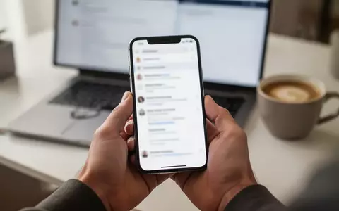 Nahaufnahme einer Hand mit einem Smartphone vor einem unscharfen Schreibtischhintergrund als Symbol für digitale Sicherheit. - Foto: über boerse-global.de