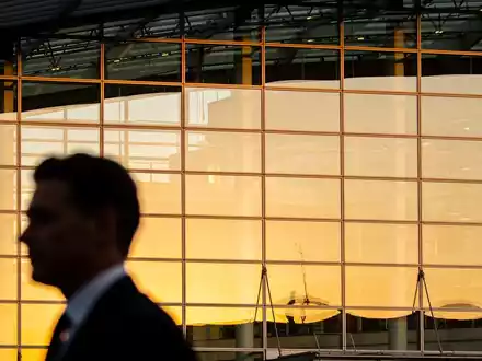 Moderne Glasfassade eines Bürogebäudes bei goldenem Licht mit der verschwommenen Silhouette einer Person im Anzug. - Foto: über boerse-global.de
