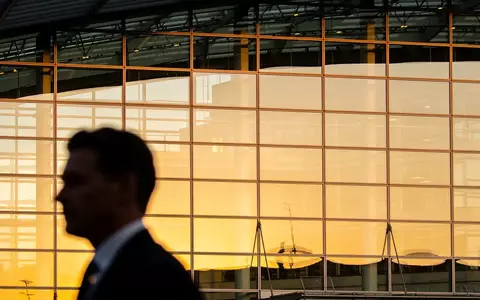 Moderne Glasfassade eines Bürogebäudes bei goldenem Licht mit der verschwommenen Silhouette einer Person im Anzug. - Foto: über boerse-global.de