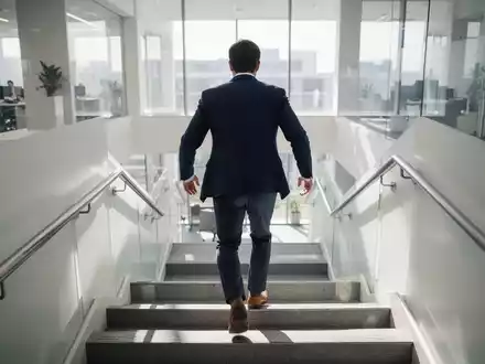 Eine Person in Business-Kleidung steigt in einem hellen Bürogebäude die Treppen hoch, um Bewegung in den Arbeitsalltag zu bringen. - Foto: über boerse-global.de