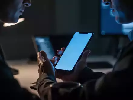 Eine Person betrachtet in einem abgedunkelten Raum ein Smartphone, während das Licht des Bildschirms ihr Gesicht beleuchtet. - Foto: über boerse-global.de