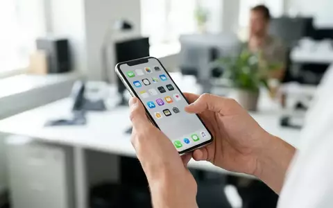 Person hält ein modernes Smartphone in einer hellen Büroumgebung, während auf dem Display eine neutrale Benutzeroberfläche zu sehen ist. - Foto: über boerse-global.de