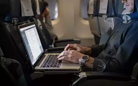 Ein Passagier sitzt in einem Flugzeug und arbeitet an einem Laptop, während das Licht des Bildschirms das Gesicht beleuchtet. - Foto: über boerse-global.de