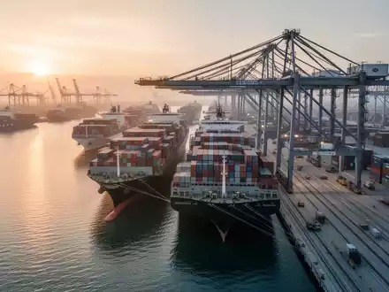 Ein moderner Industriehafen mit Containerschiffen und Kränen bei Sonnenuntergang als Symbol für internationalen Handel. - Foto: über boerse-global.de