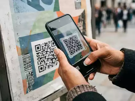 Eine Person scannt mit einem Smartphone einen QR-Code auf einem öffentlichen Plakat in einer städtischen Umgebung. - Foto: über boerse-global.de