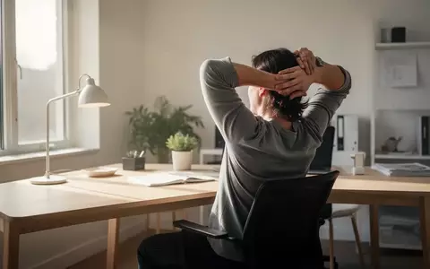 Person beim Dehnen des Rückens an einem Schreibtisch im Homeoffice bei natürlichem Tageslicht. - Foto: über boerse-global.de