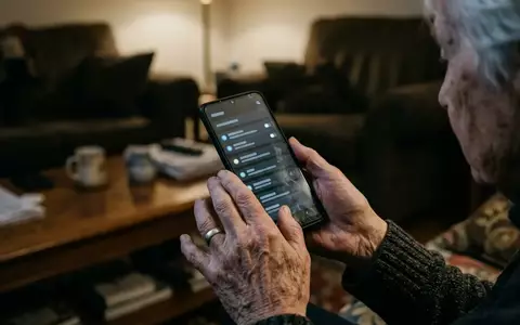 Nahaufnahme der Hände eines Senioren, der ein Smartphone in einem abgedunkelten Raum hält, während er auf den Bildschirm blickt. - Foto: über boerse-global.de