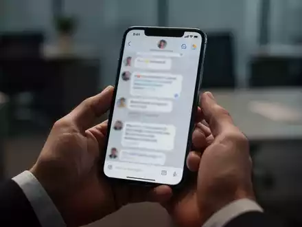Ein modernes Smartphone in der Hand einer Person, das eine Chat-Oberfläche in einer professionellen Büroumgebung zeigt. - Foto: über boerse-global.de
