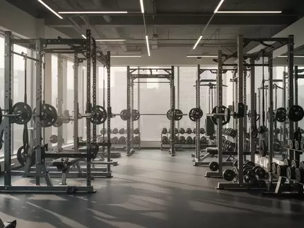 Modernes Fitnessstudio mit hochwertigen Kraftsportgeräten und Hantelständern in einer hellen, aufgeräumten Trainingsumgebung. - Foto: über boerse-global.de
