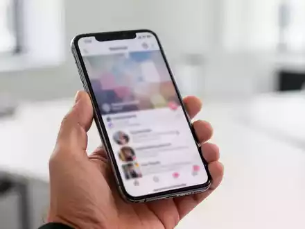 Eine Person hält ein Smartphone in einer hellen Büroumgebung, während sie durch einen sozialen Feed scrollt. - Foto: über boerse-global.de