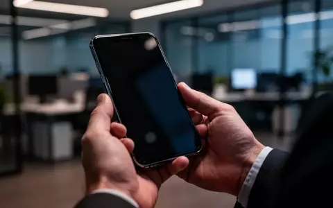 Nahaufnahme einer Hand, die ein Smartphone in einem modernen Büro hält, als Symbol für die Bedrohung durch Banking-Malware. - Foto: über boerse-global.de