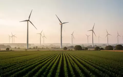 Moderne Windkraftanlagen in einer weitläufigen ländlichen Agrarlandschaft bei Sonnenuntergang. - Foto: über boerse-global.de