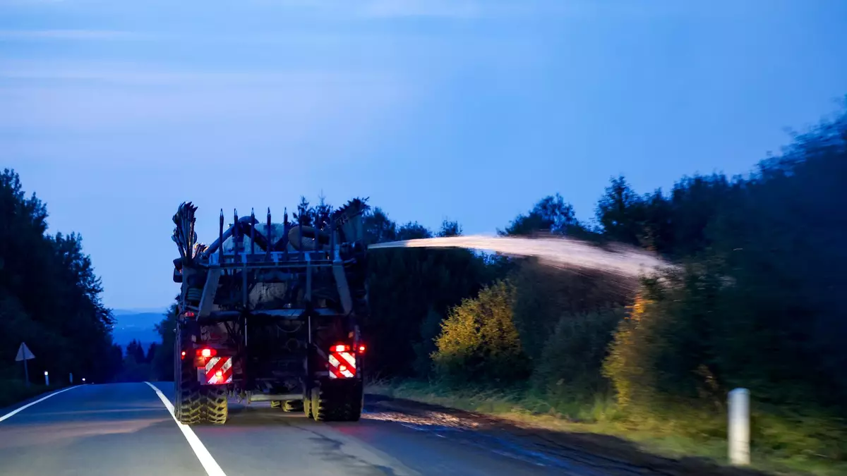 Ein landwirtschaftliches Fahrzeug wässert den Straßenrand mit Wasser aus dem Tank hinter seinem Traktor gegen die Flammen.  - Bild: Thomas Banneyer/dpa
