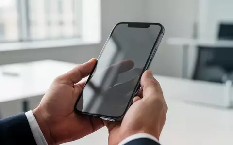 Eine Nahaufnahme einer Hand, die ein modernes Smartphone in einer hellen, professionellen Büroumgebung hält. - Foto: über boerse-global.de
