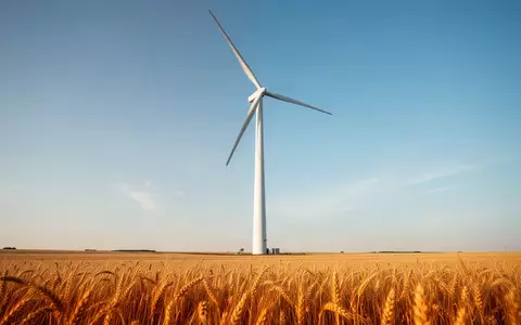 Eine moderne Windkraftanlage in einem weiten goldenen Weizenfeld unter blauem Himmel. - Foto: über boerse-global.de
