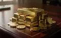 Nahaufnahme von Goldbarren und Goldmünzen auf einer dunklen Holzoberfläche bei natürlichem Licht. - Foto: über boerse-global.de