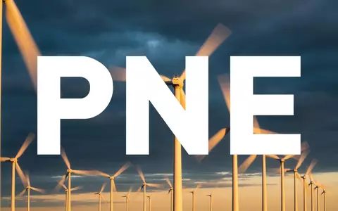 Moderne Windkraftanlagen in einer weiten Landschaft unter einem düsteren, bewölkten Himmel bei Sonnenuntergang. - Foto: über boerse-global.de