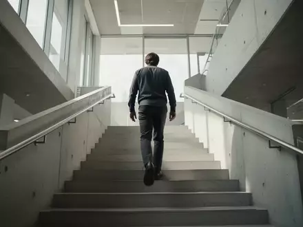 Eine Person steigt eine moderne, helle Betontreppe in einem Gebäude hinauf. - Foto: über boerse-global.de