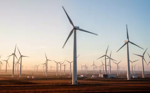 Moderne Windkraftanlagen in einer weitläufigen Landschaft bei Sonnenaufgang. - Foto: über boerse-global.de
