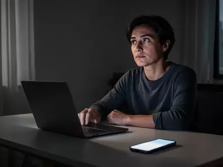Eine Person sitzt nachdenklich an einem Schreibtisch vor einem Laptop, während ein Smartphone daneben liegt. - Foto: über boerse-global.de