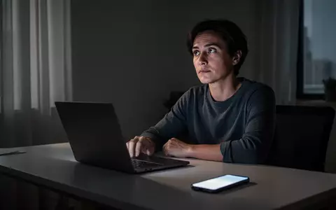 Eine Person sitzt nachdenklich an einem Schreibtisch vor einem Laptop, während ein Smartphone daneben liegt. - Foto: über boerse-global.de