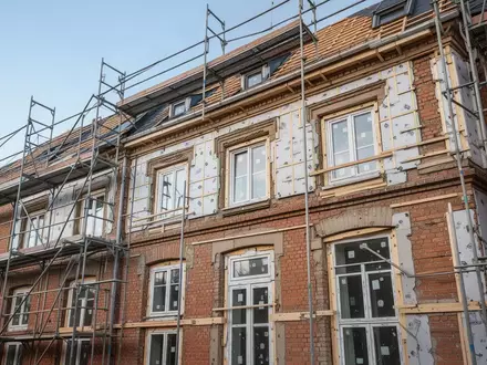 Ein saniertes Altbaugebäude mit Gerüst an einer Straßenecke bei Tageslicht. - Foto: über boerse-global.de