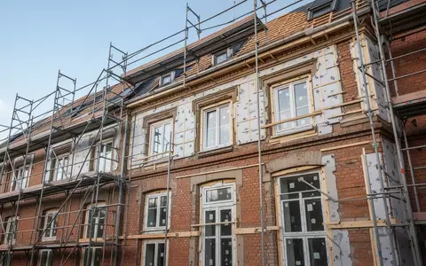 Ein saniertes Altbaugebäude mit Gerüst an einer Straßenecke bei Tageslicht. - Foto: über boerse-global.de