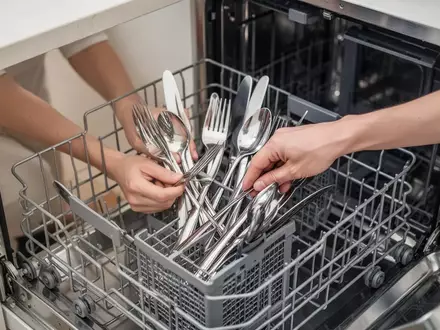 Hände beim ordnungsgemäßen Einräumen von Besteck in eine Geschirrspülmaschine in einer modernen Küche. - Foto: über boerse-global.de