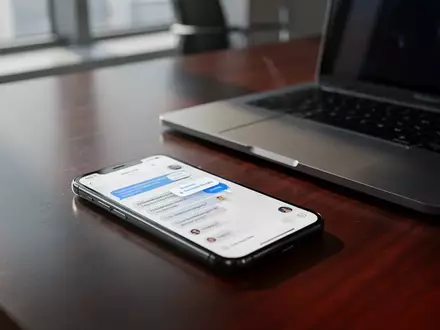 Ein Smartphone auf einem Büroschreibtisch neben einem Laptop, das eine Chat-Nachricht anzeigt, während im Hintergrund ein unscharfes Büro zu sehen ist. - Foto: über boerse-global.de