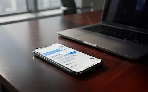 Ein Smartphone auf einem Büroschreibtisch neben einem Laptop, das eine Chat-Nachricht anzeigt, während im Hintergrund ein unscharfes Büro zu sehen ist. - Foto: über boerse-global.de