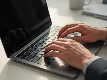 Nahaufnahme einer Person, die an einem Laptop arbeitet, in einer hellen, professionellen Büroumgebung. - Foto: über boerse-global.de