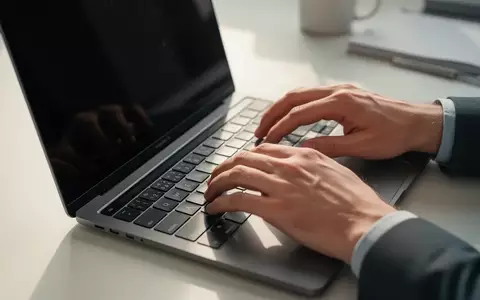 Nahaufnahme einer Person, die an einem Laptop arbeitet, in einer hellen, professionellen Büroumgebung. - Foto: über boerse-global.de