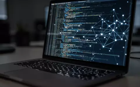 Ein Laptop-Bildschirm mit verschwommenem Programmiercode und Netzwerkverbindungen in einem abgedunkelten Büro. - Foto: über boerse-global.de